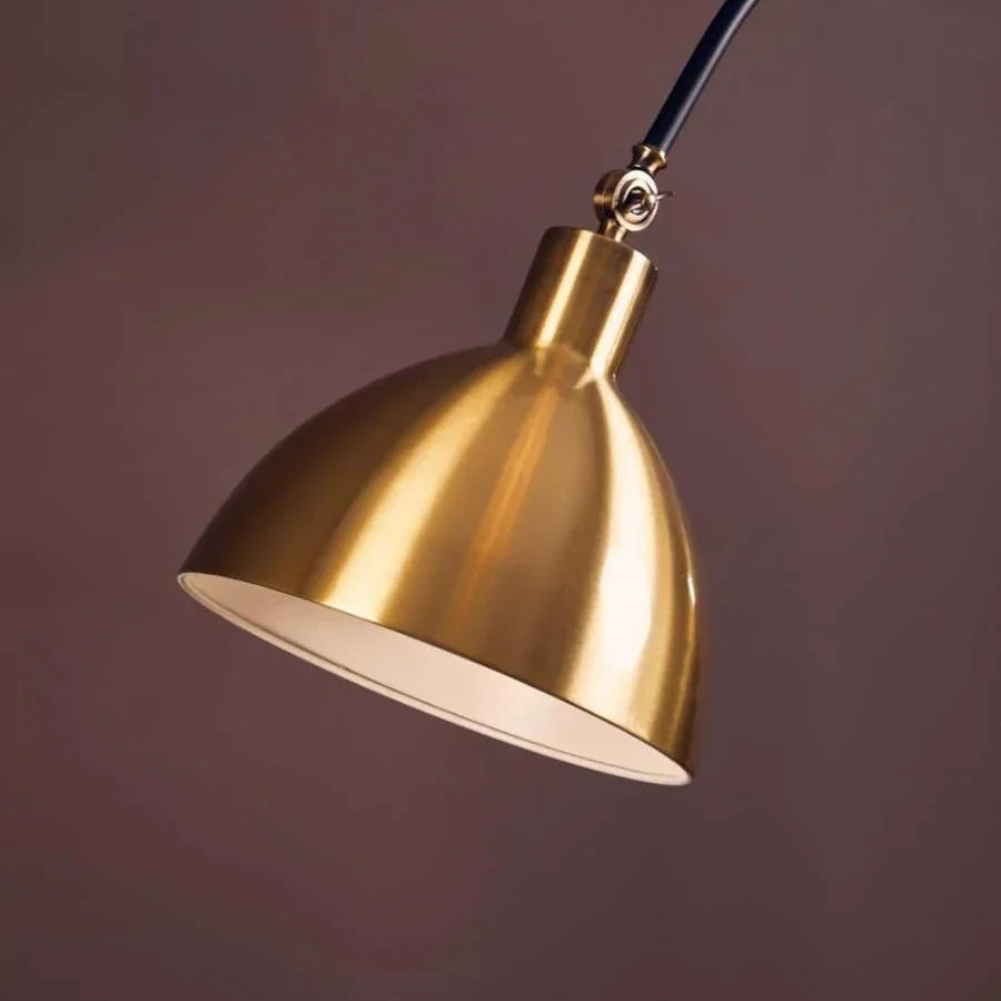 Brass metal arc floor lamp with curved black arm against a brown background