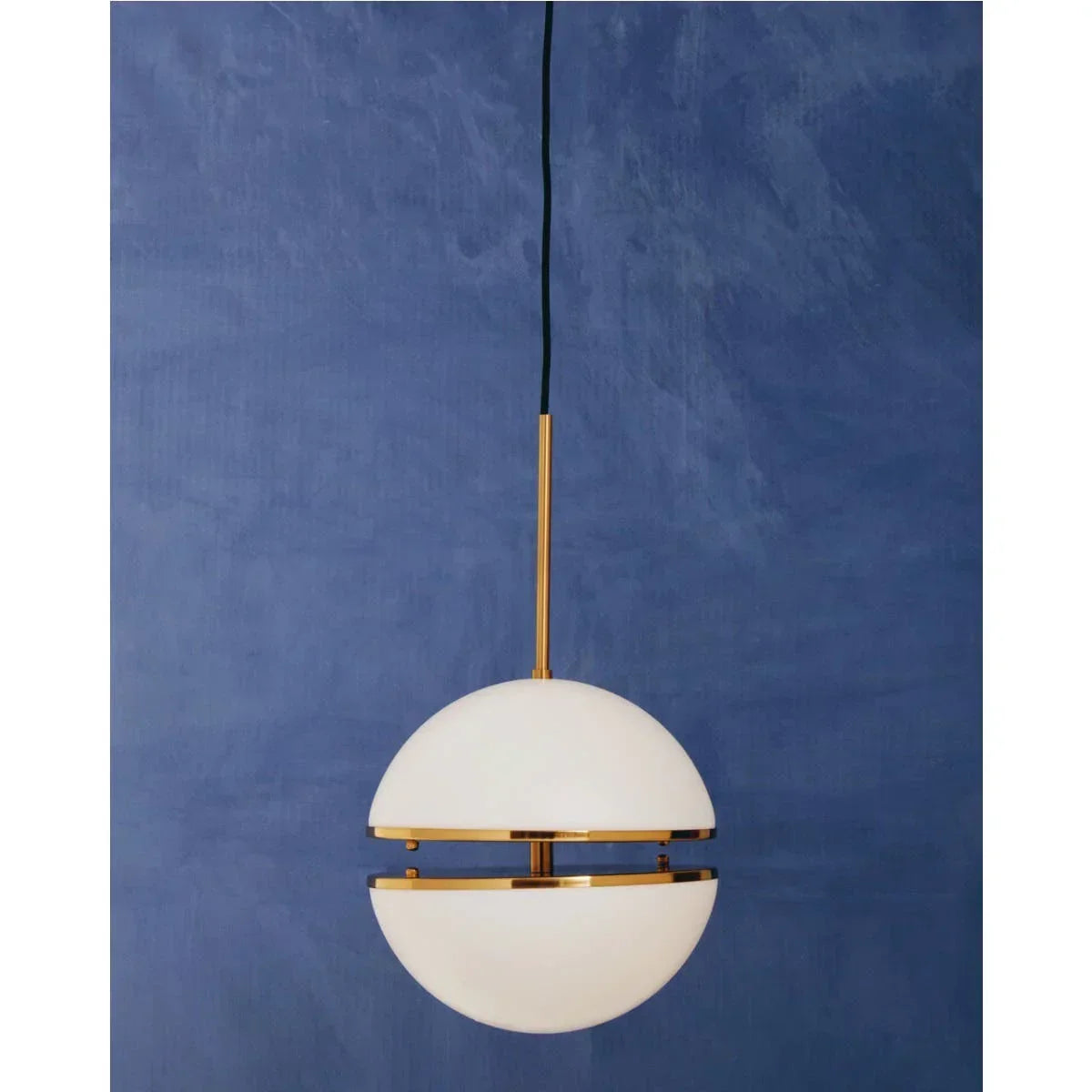 Modern globe pendant light with brass and white glass shade against blue wall