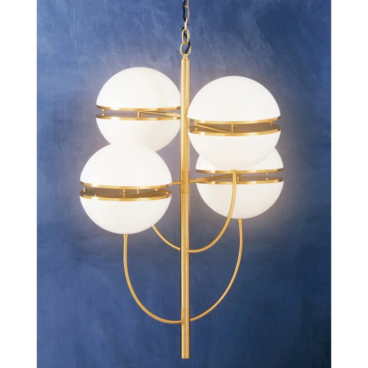 Modern gold chandelier with four white globe lights against a blue wall