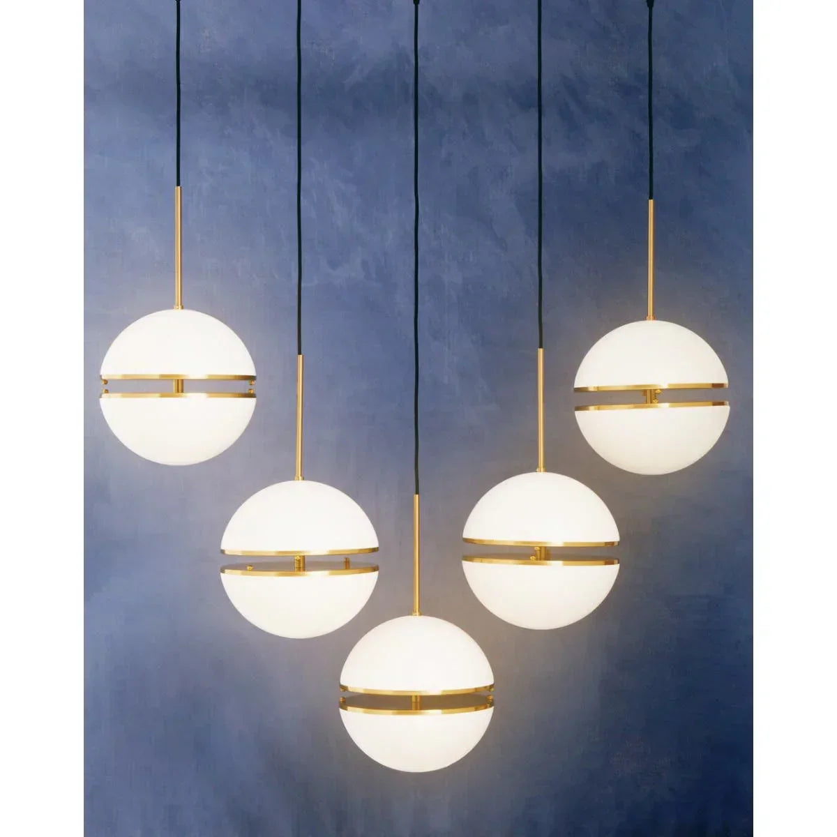 Five globe pendant lights with gold accents against a blue wall