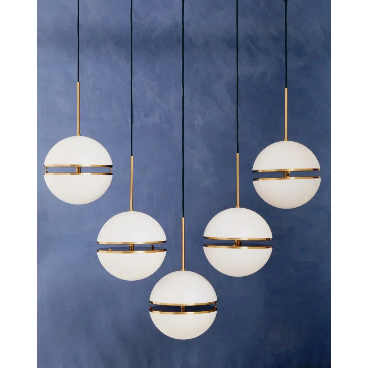 Five modern globe pendant lights with gold accents against blue wall
