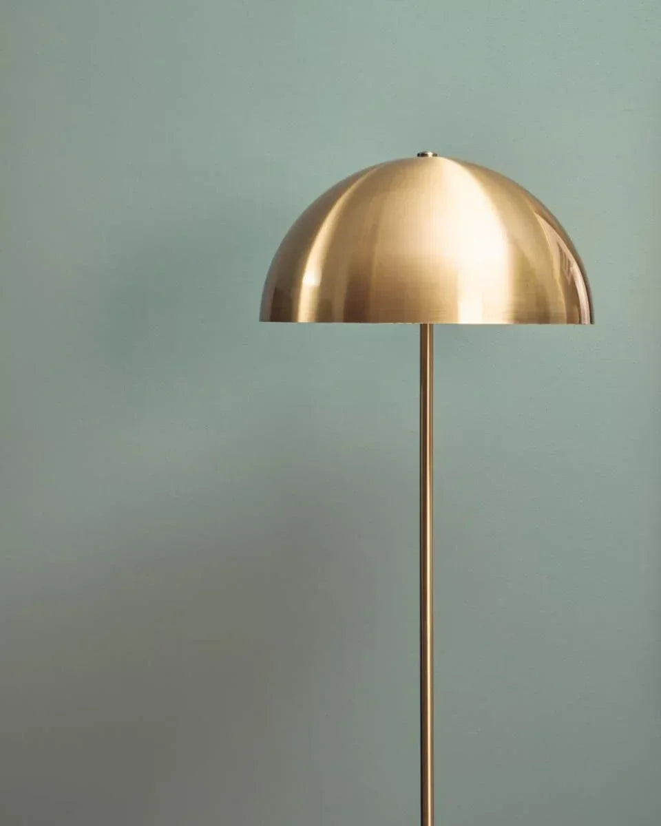 Brushed gold floor lamp with dome shade against light blue wall
