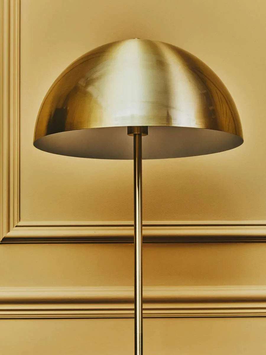 Gold metal floor lamp with dome shade against a decorative beige wall panel