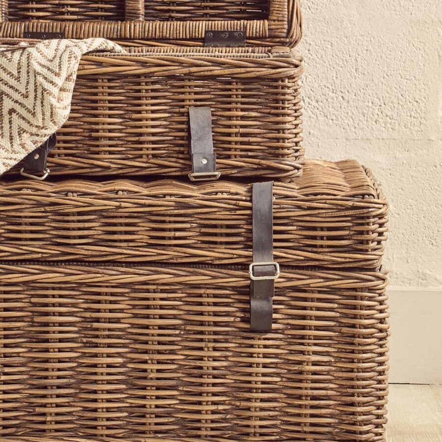 Stacked wicker storage baskets with leather straps on wooden floor
