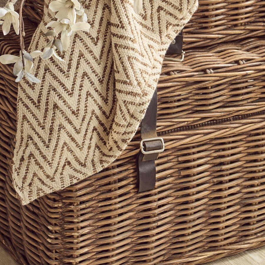 Wicker storage basket with leather straps, chevron pattern throw and artificial flowers