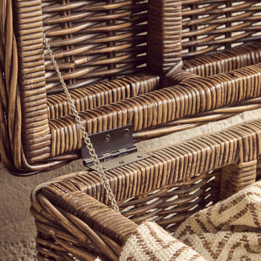 Closeup of open wicker storage basket with metal hinge and patterned throw blanket inside