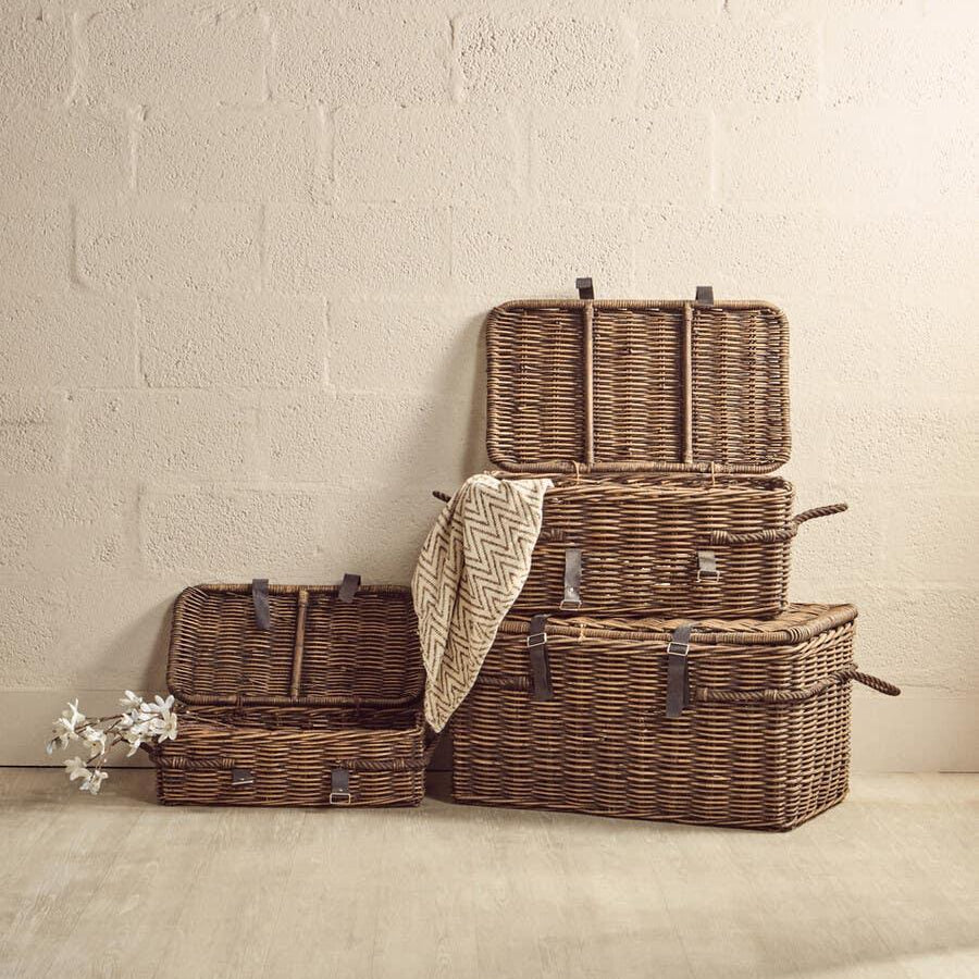 Set of three wicker storage baskets with lids and leather straps on wooden floor