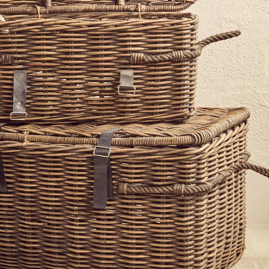 Stacked wicker storage baskets with rope handles and leather buckles on wood floor