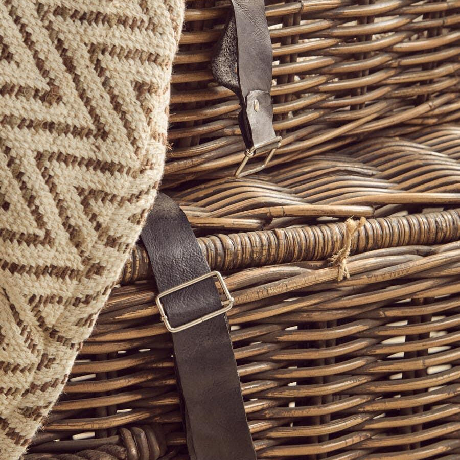 Wicker storage trunk with leather straps and textured beige throw draped over side