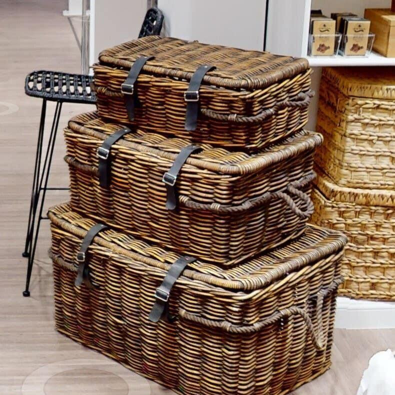 Stacked wicker storage baskets with lids and leather straps in showroom setting
