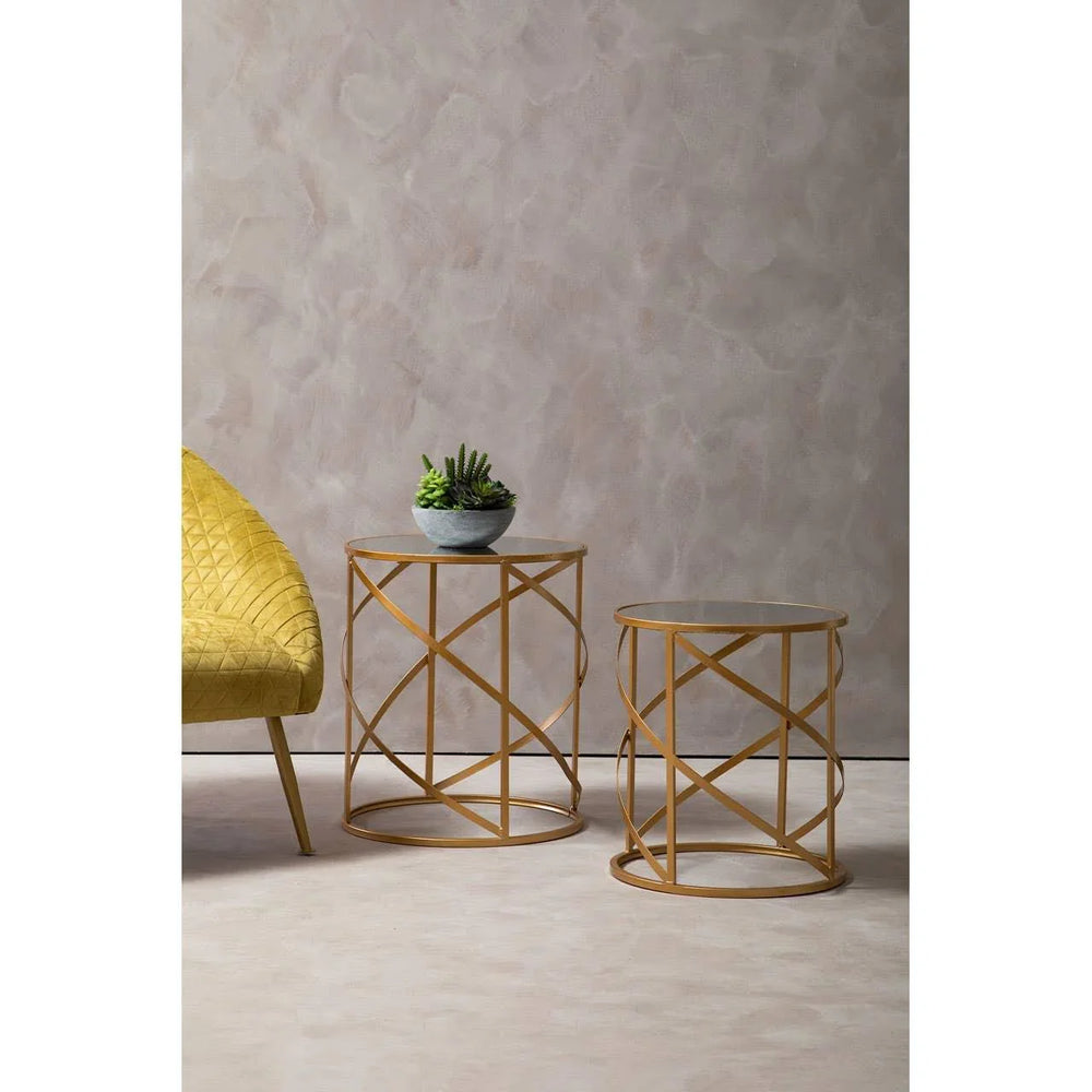 Gold metal side tables with glass tops beside a yellow upholstered chair and potted plant