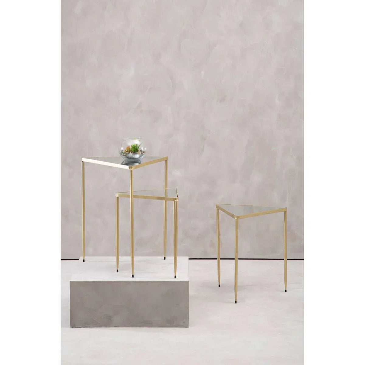 Set of three glass top nesting tables with gold metal frames on light background