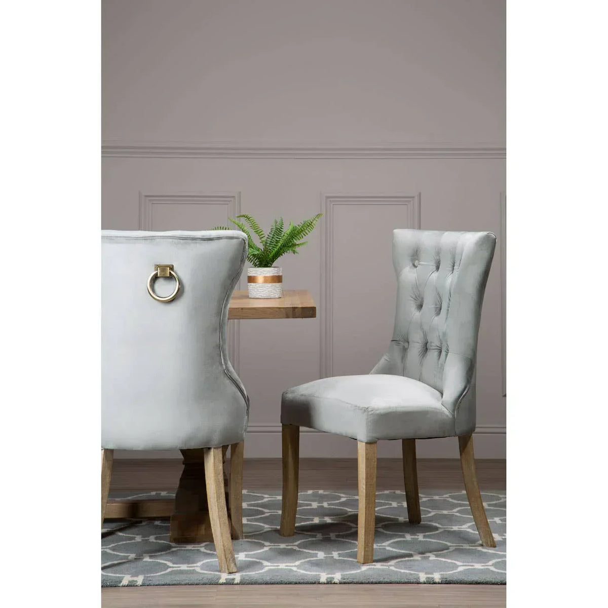 Grey velvet dining chair with button tufting and wooden legs beside wooden dining table