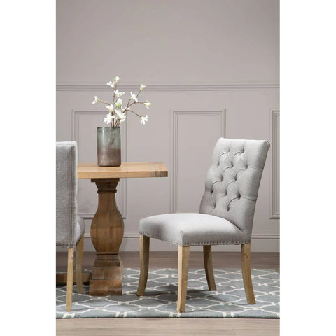 Light grey upholstered dining chair with button tufting beside wooden dining table