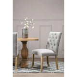 Light grey upholstered dining chair with button tufting beside wooden dining table