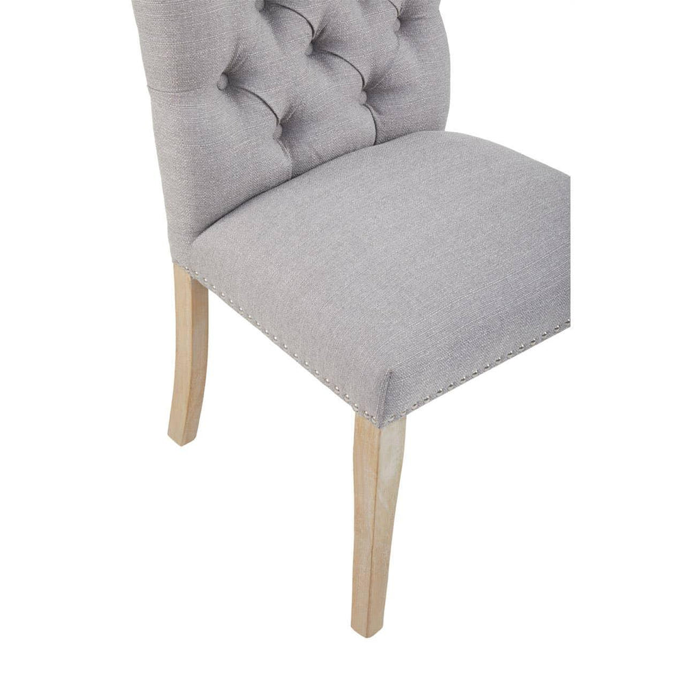 Grey upholstered dining chair with button-tufted back and light wood legs, corner view