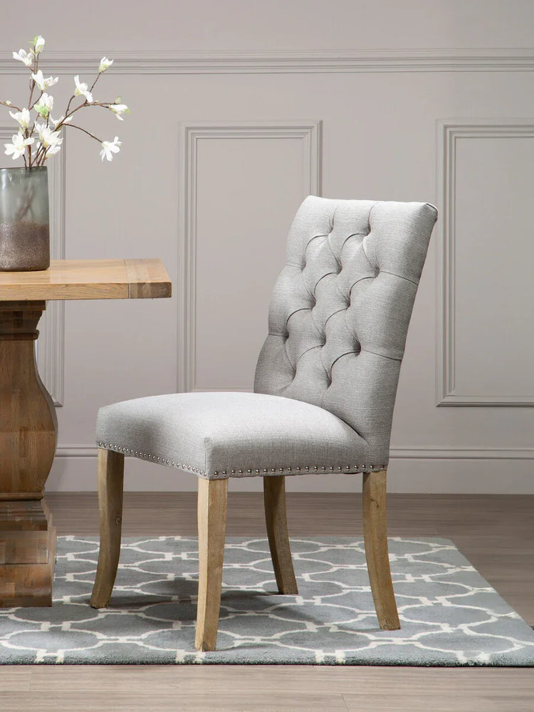 Grey upholstered dining chair with button back and wooden legs on patterned rug