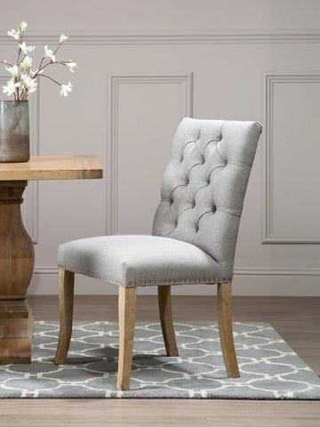 Grey upholstered dining chair with button back and wooden legs on patterned rug