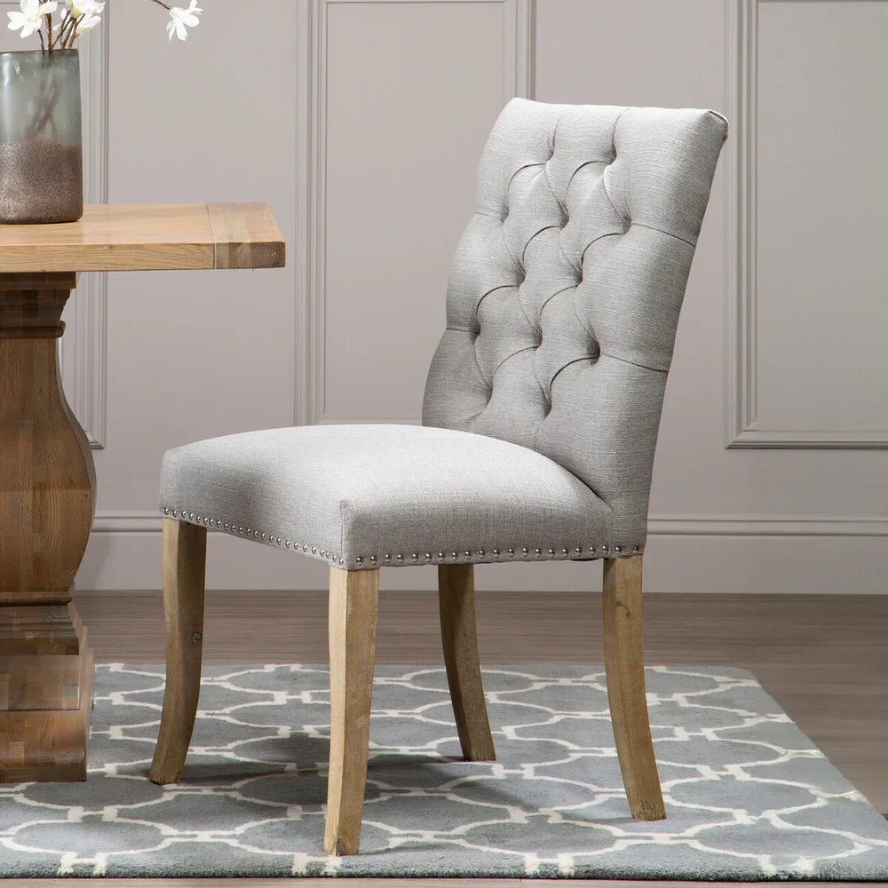 Grey upholstered dining chair with button tufted back and wooden legs on patterned rug