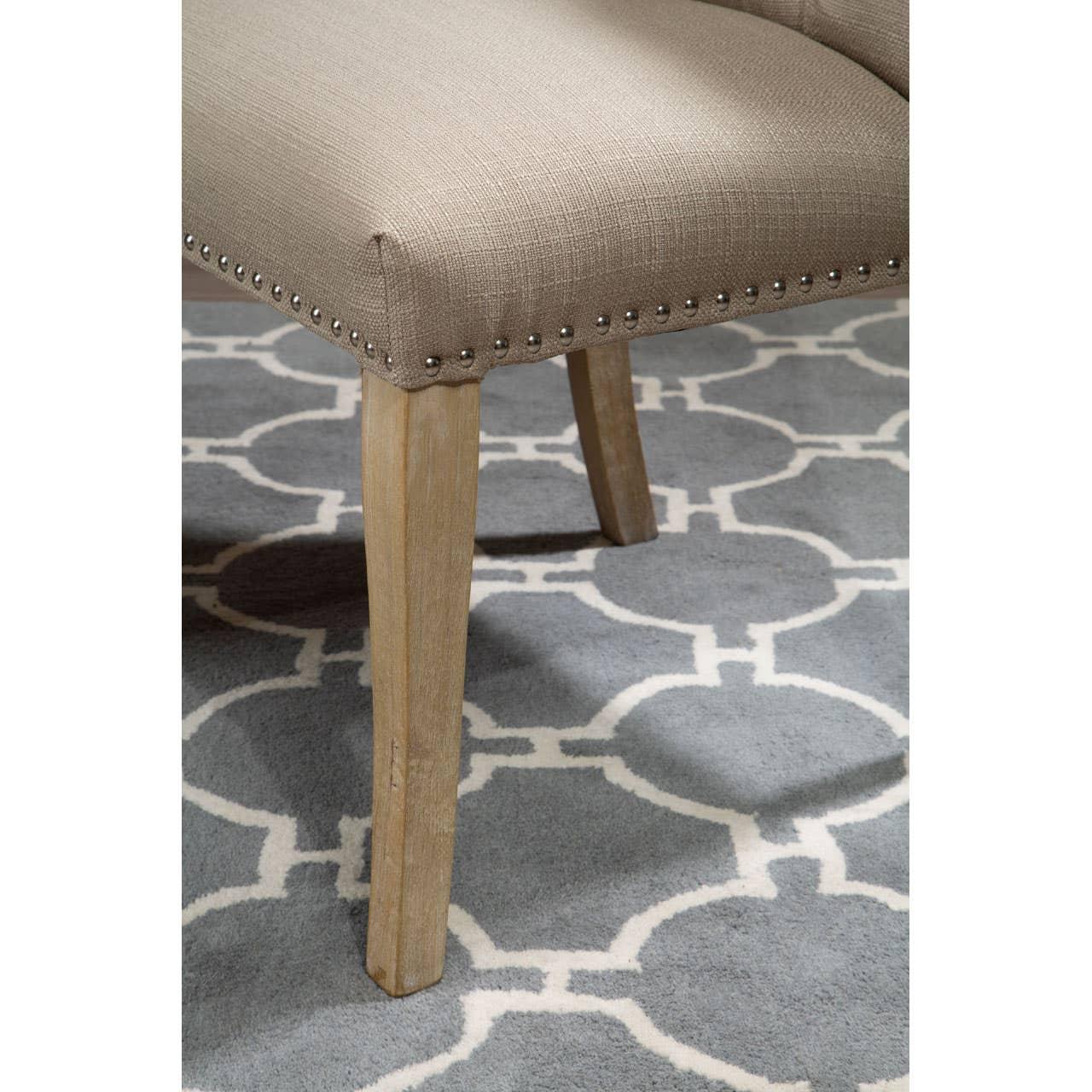 Beige upholstered dining chair with nailhead trim and wooden legs on patterned rug