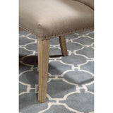 Beige upholstered dining chair with nailhead trim and wooden legs on patterned rug