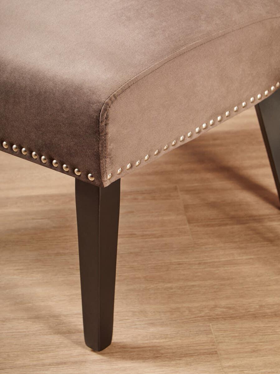Upholstered chair seat with studded trim and dark wooden legs on wood flooring