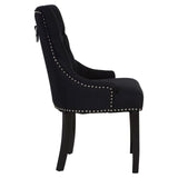 Side angle of black upholstered dining chair with metal stud detailing and dark wooden legs