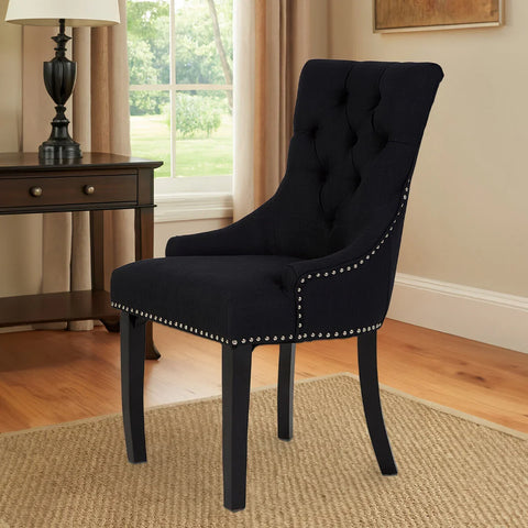 Black upholstered dining chair with button tufting and silver nailhead trim on carpet