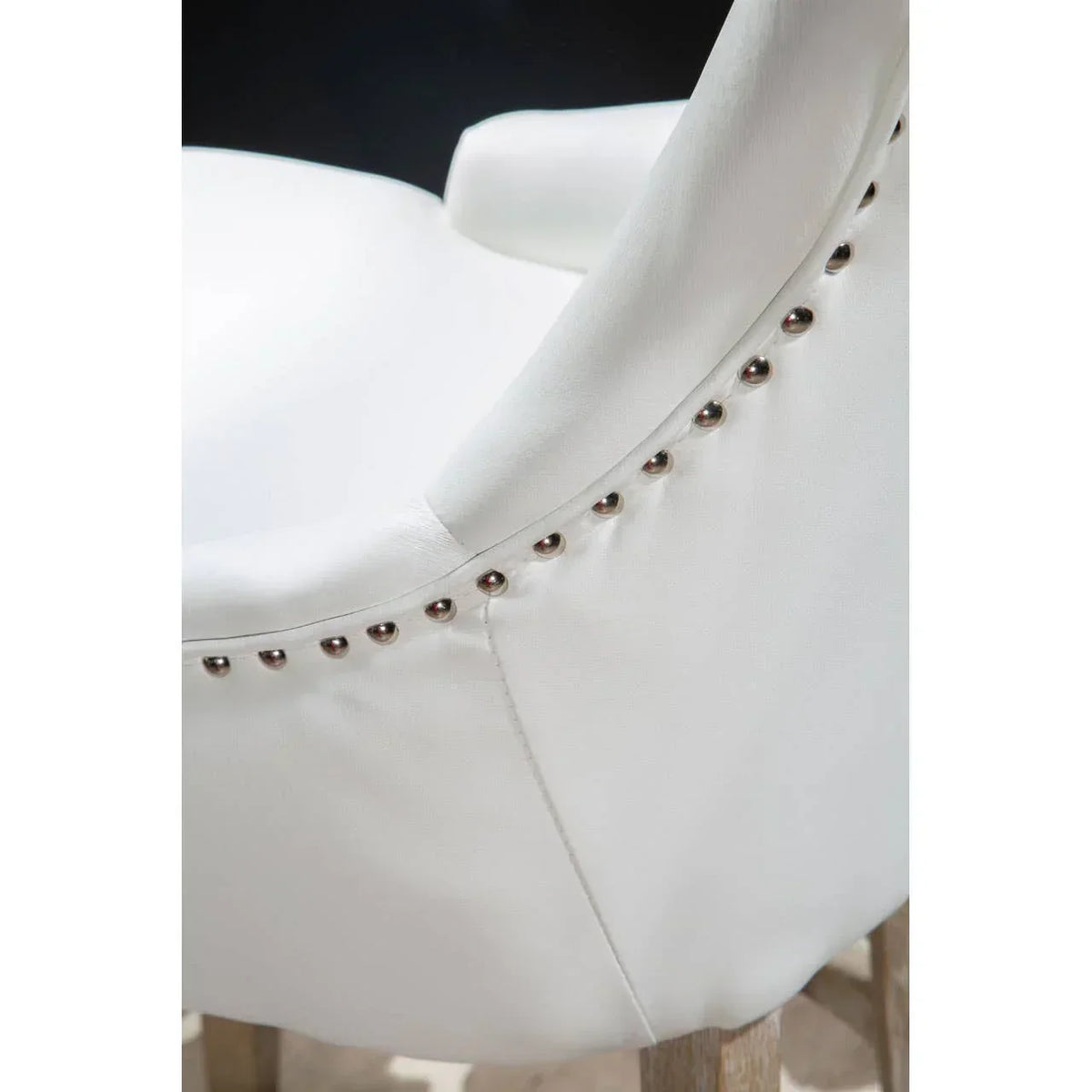 White upholstered dining chair with silver stud detailing and wooden legs, close view