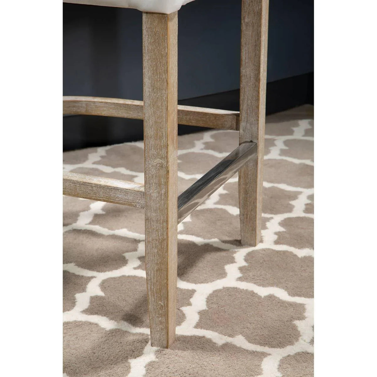 Light wood bar stool legs with metal footrest on patterned beige rug