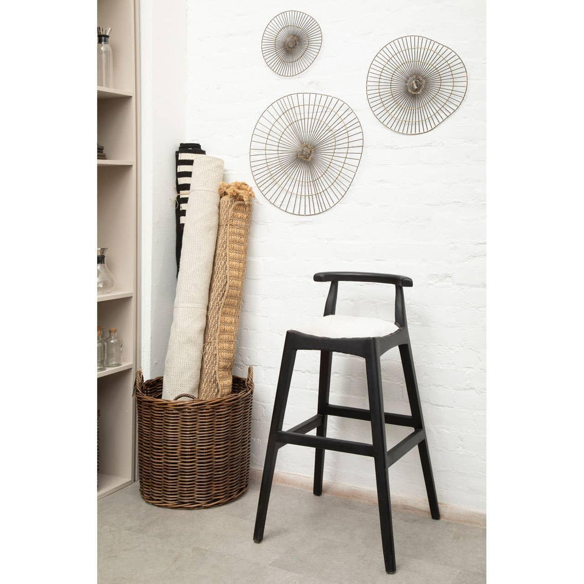 Black wooden bar stool with white seat beside wicker basket and rolled rugs in modern room