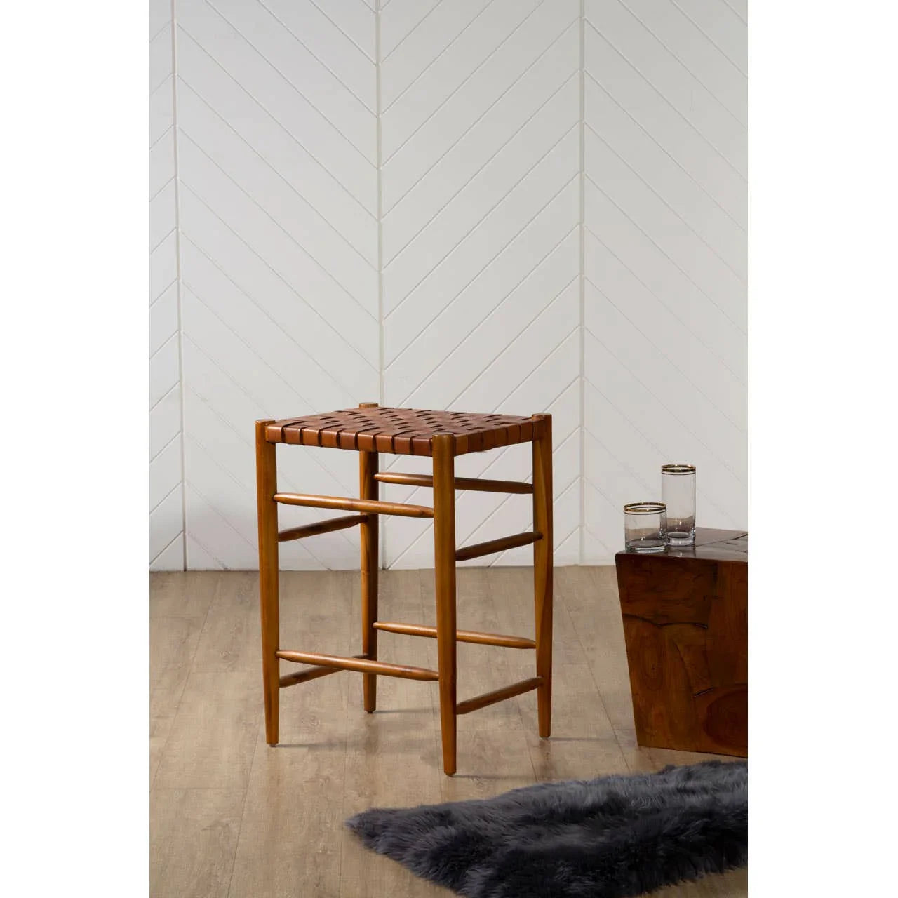 Wooden bar stool with woven leather seat on wood floor near side table and glasses