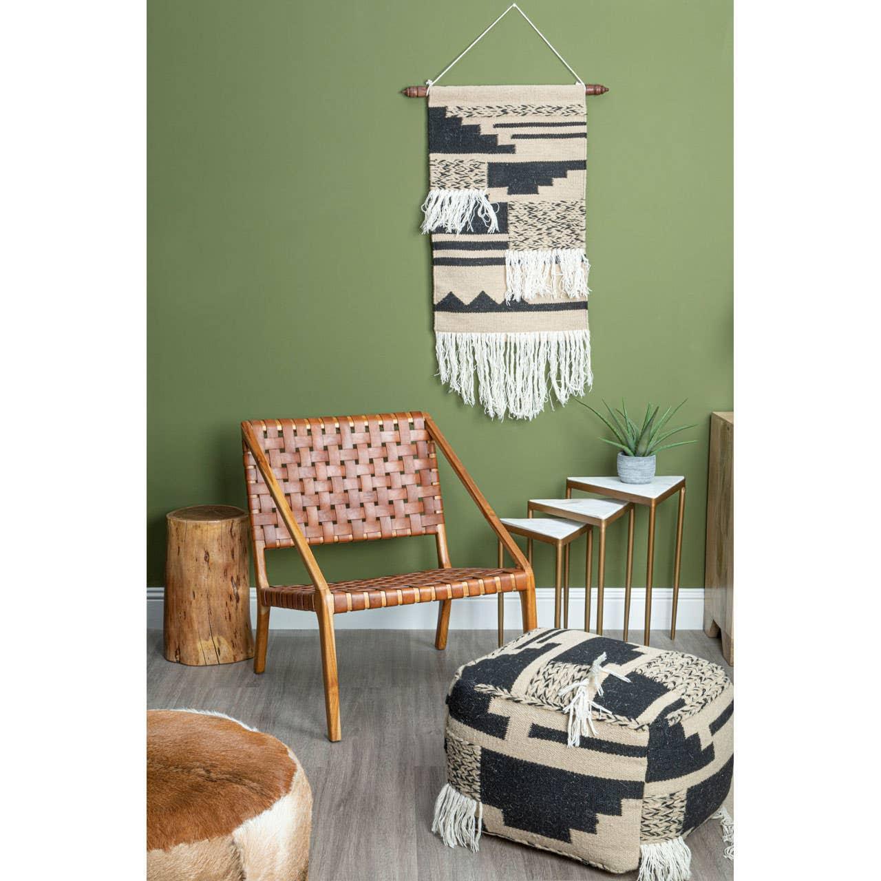 Woven leather accent chair with wooden frame beside patterned pouffe and nesting tables