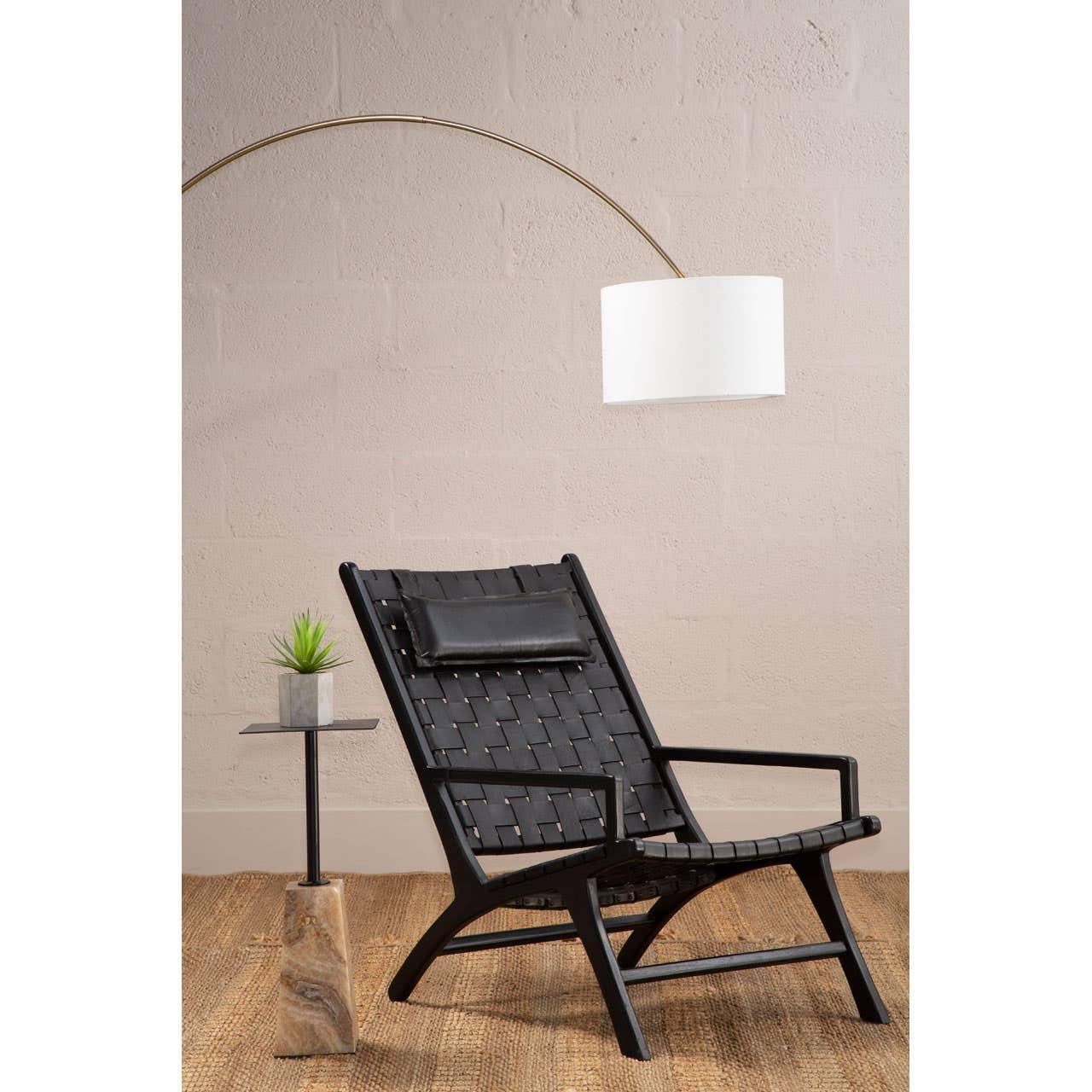Black woven lounge chair with cushioned headrest beside side table and floor lamp