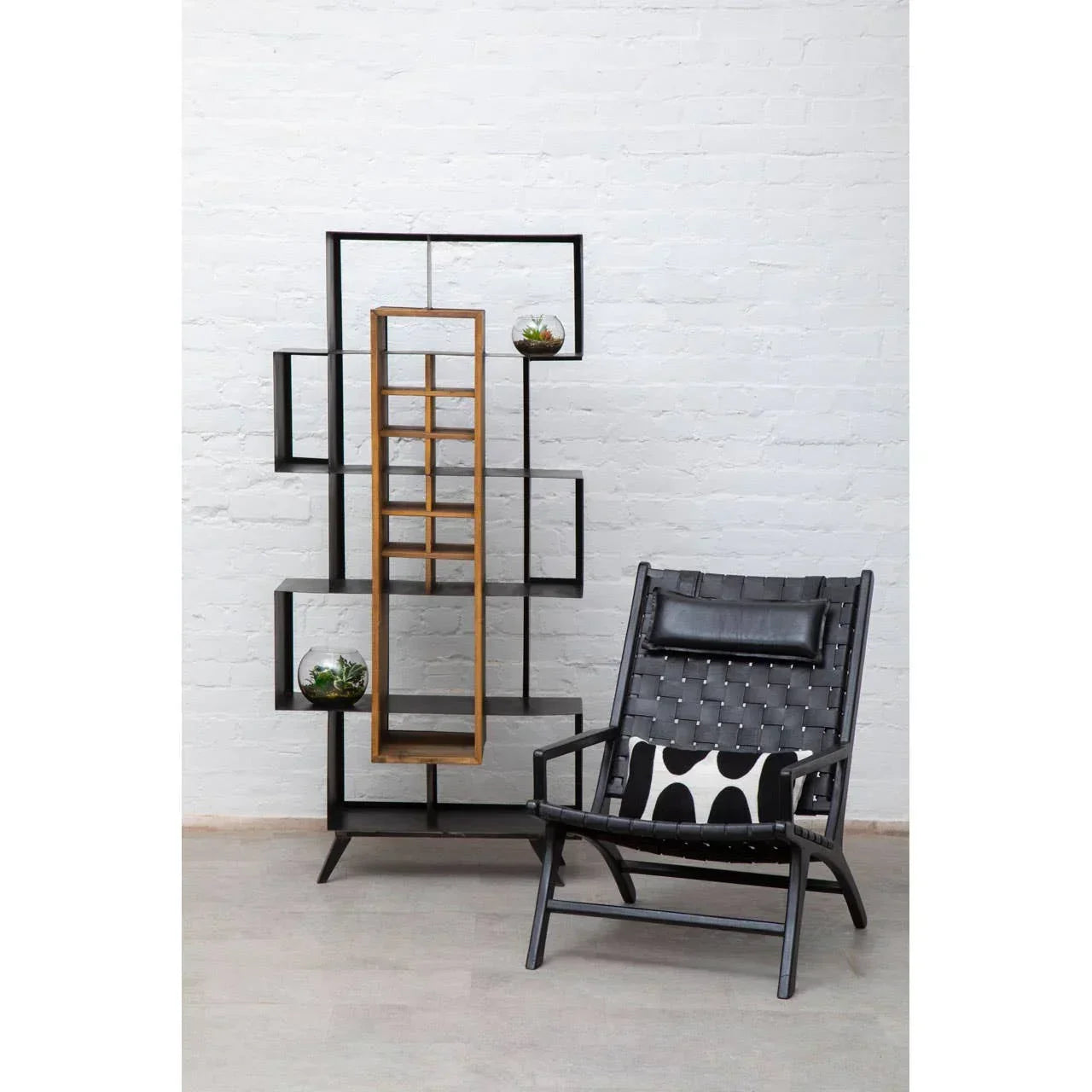Black woven accent chair with cushion beside modern geometric shelving unit against white wall