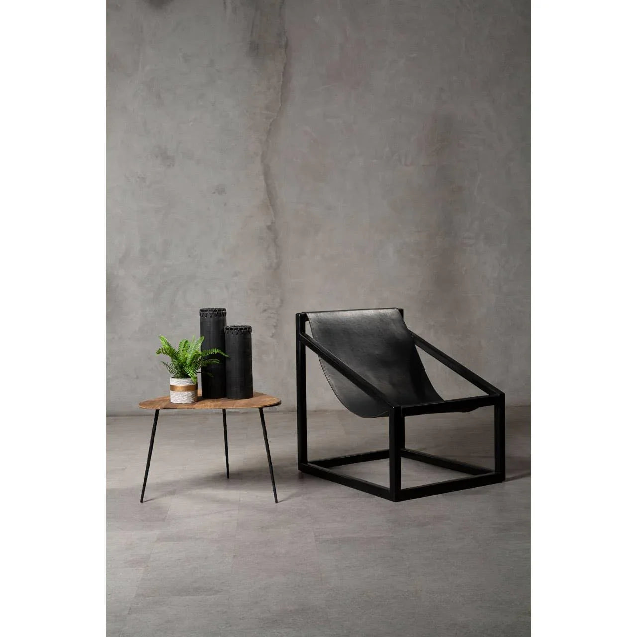 Black leather accent chair with metal frame beside round wood side table and plant decor