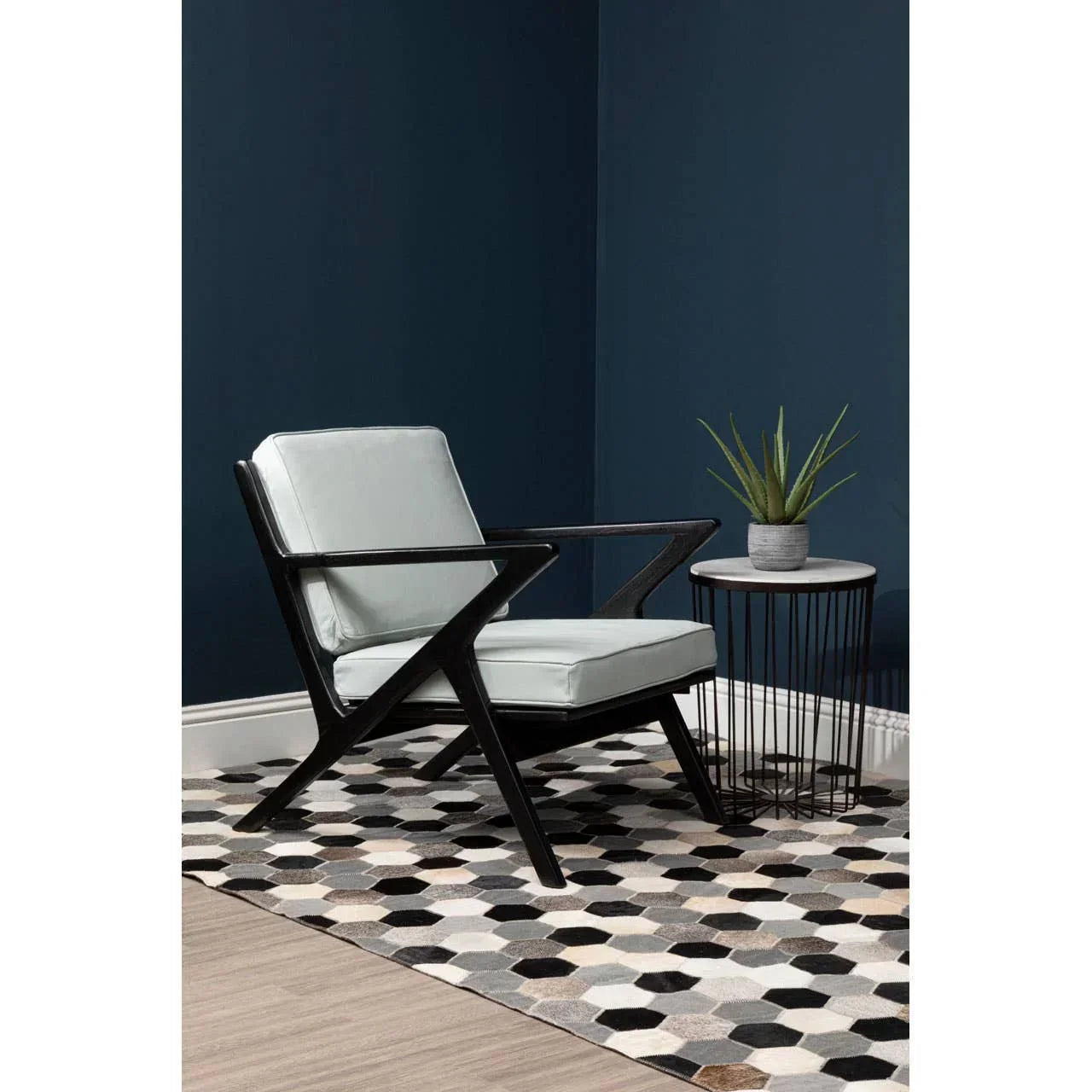 Modern accent chair with light upholstery and black frame beside round side table on geometric rug