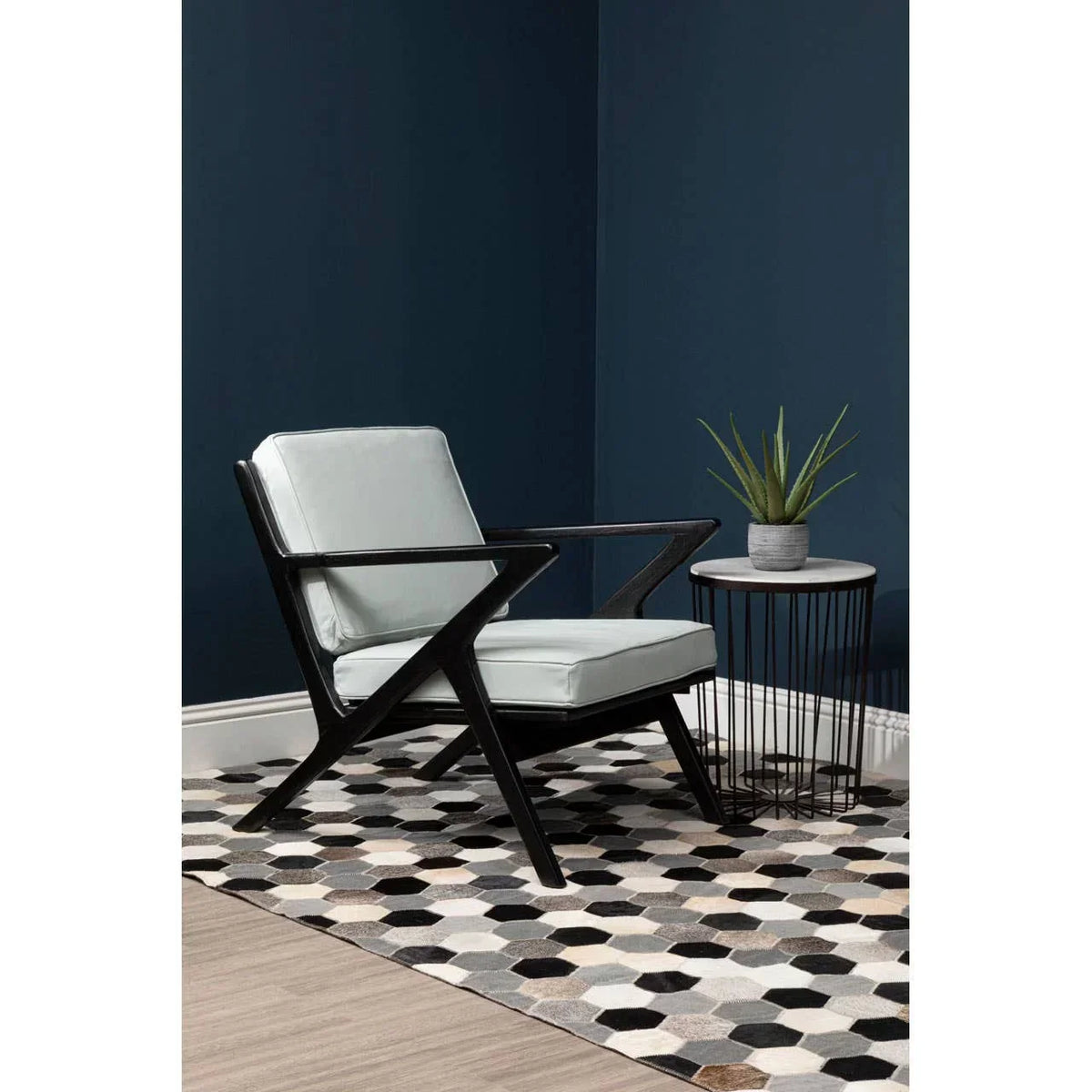 Modern accent chair with light upholstery and black frame beside round side table on geometric rug