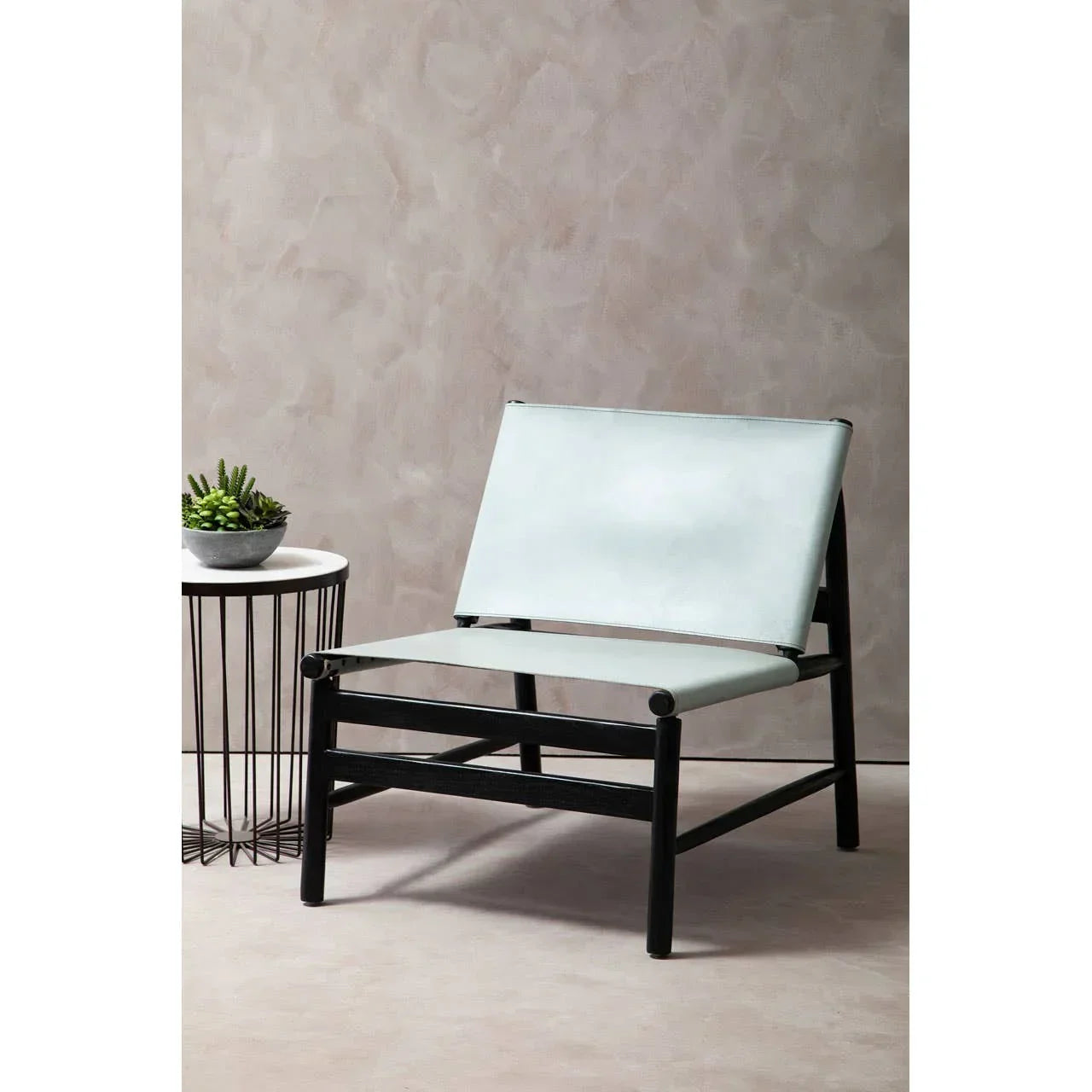 Modern lounge chair with black frame and light grey seat beside side table with plant
