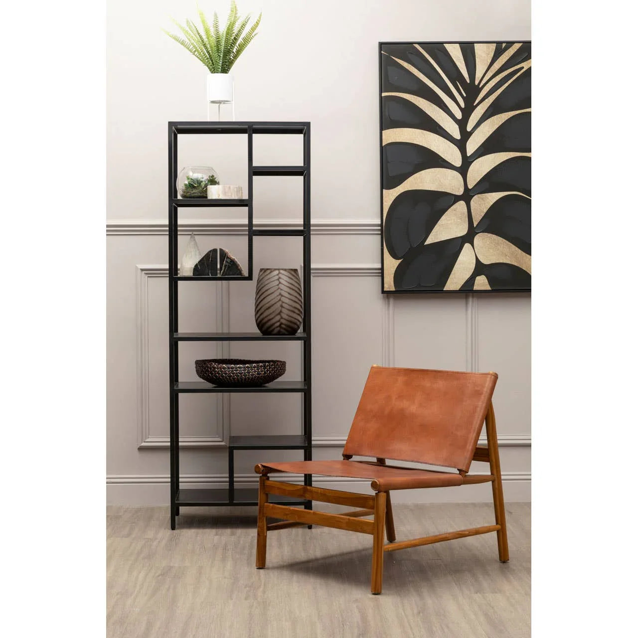 Brown leather accent chair with wooden frame beside black metal shelving unit and decorative art