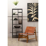 Brown leather accent chair with wooden frame beside black metal shelving unit and decorative art