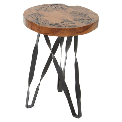 Round teak wood stool featuring intricate carvings on the top surface, supported by a sleek black metal base with curved legs. The natural wood finish highlights the grain and texture of the teak