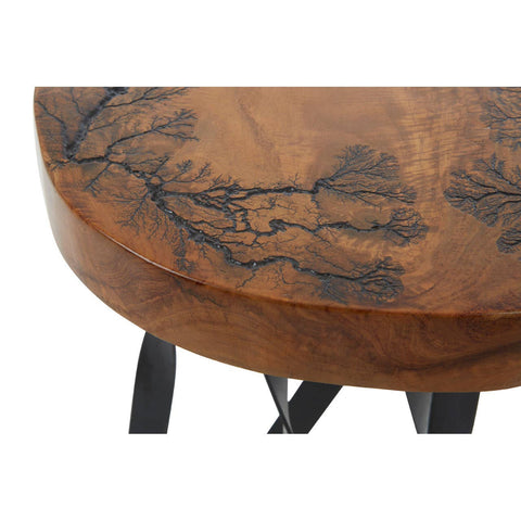 Round teak wood stool featuring intricate carvings on the surface, showcasing natural wood grain patterns and a rich brown finish. The stool is supported by black legs, providing a modern contrast to the organic design
