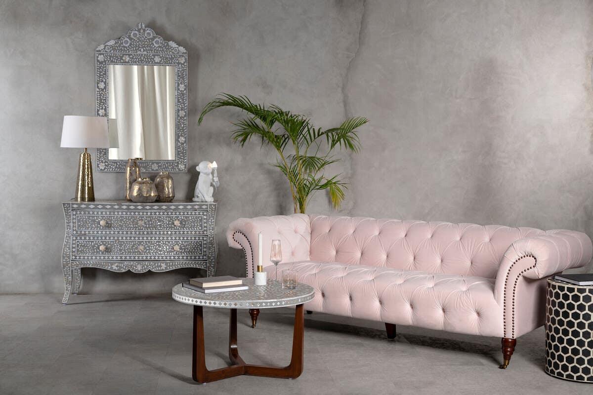 Pink tufted velvet sofa with button detail beside decorative bone inlay sideboard and mirror
