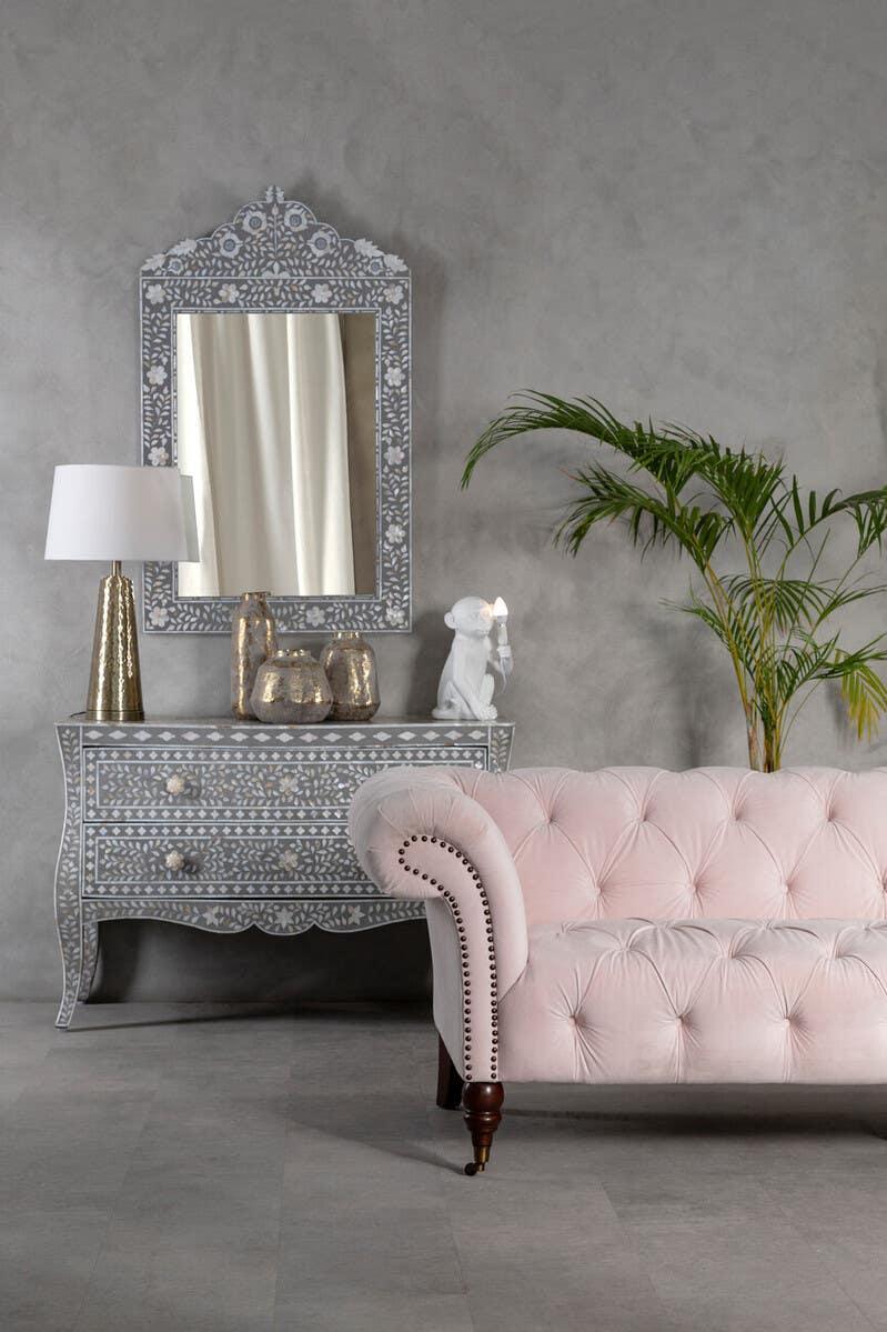 Pink velvet Chesterfield sofa with nailhead trim beside grey bone inlay console table and mirror
