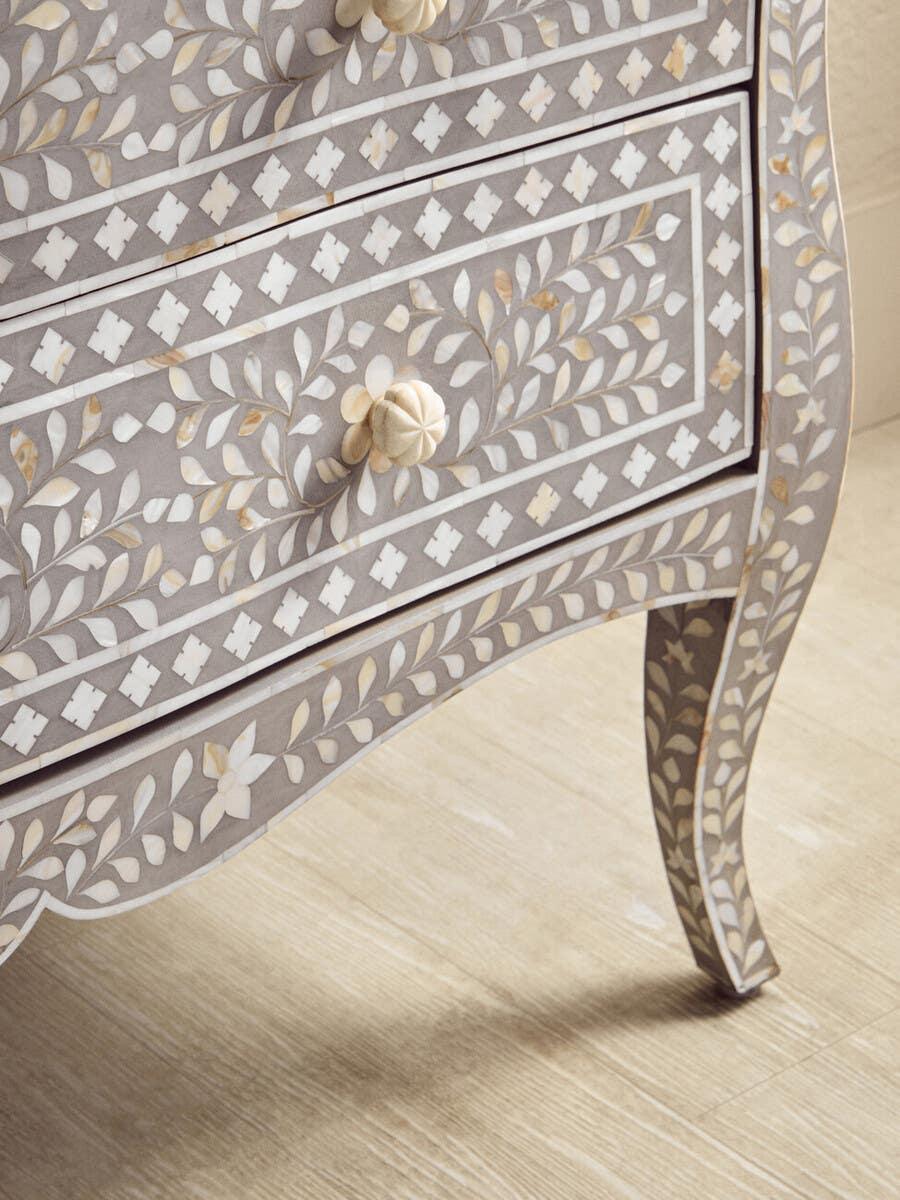 Grey bone inlay chest of drawers with floral pattern and carved handles on wood floor