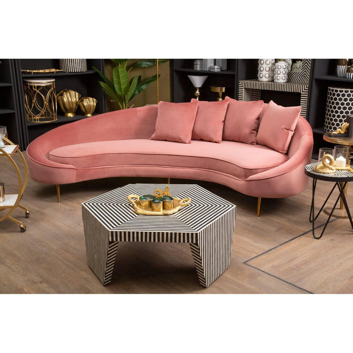 Curved pink velvet sofa with gold legs and cushions beside a striped coffee table in living room