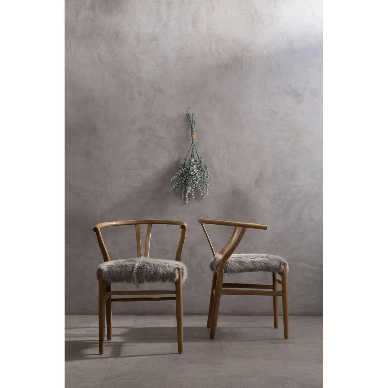 Pair of wooden dining chairs with grey faux fur seat pads against a plain wall