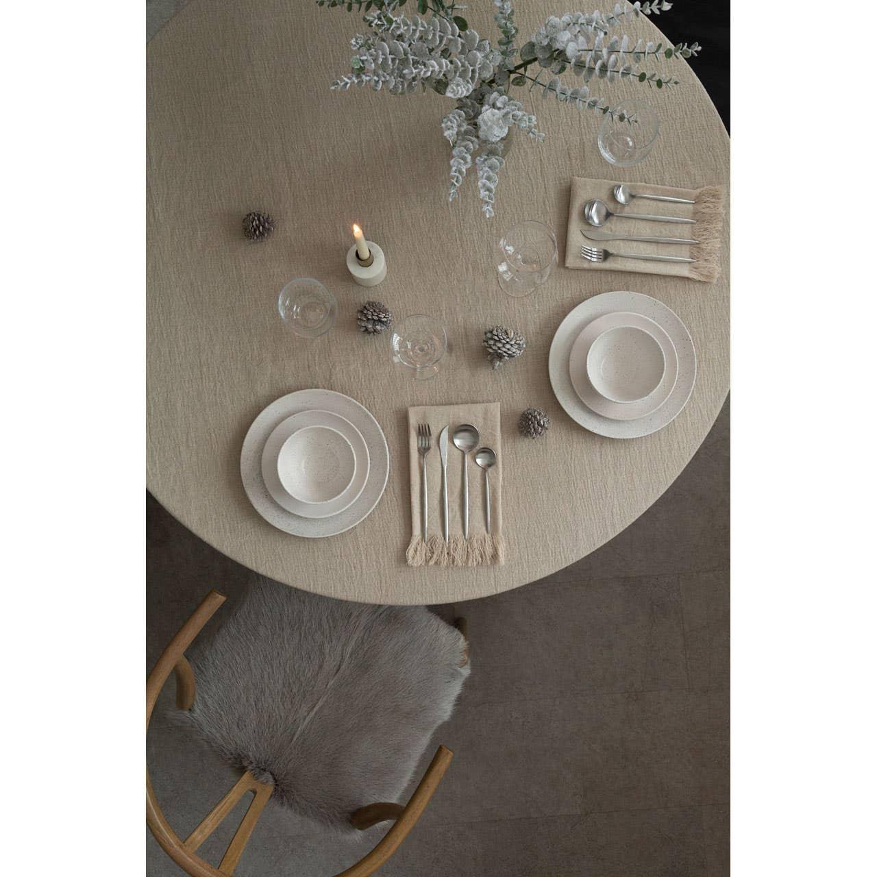 Round dining table with neutral tableware, cutlery, glassware, and floral centrepiece