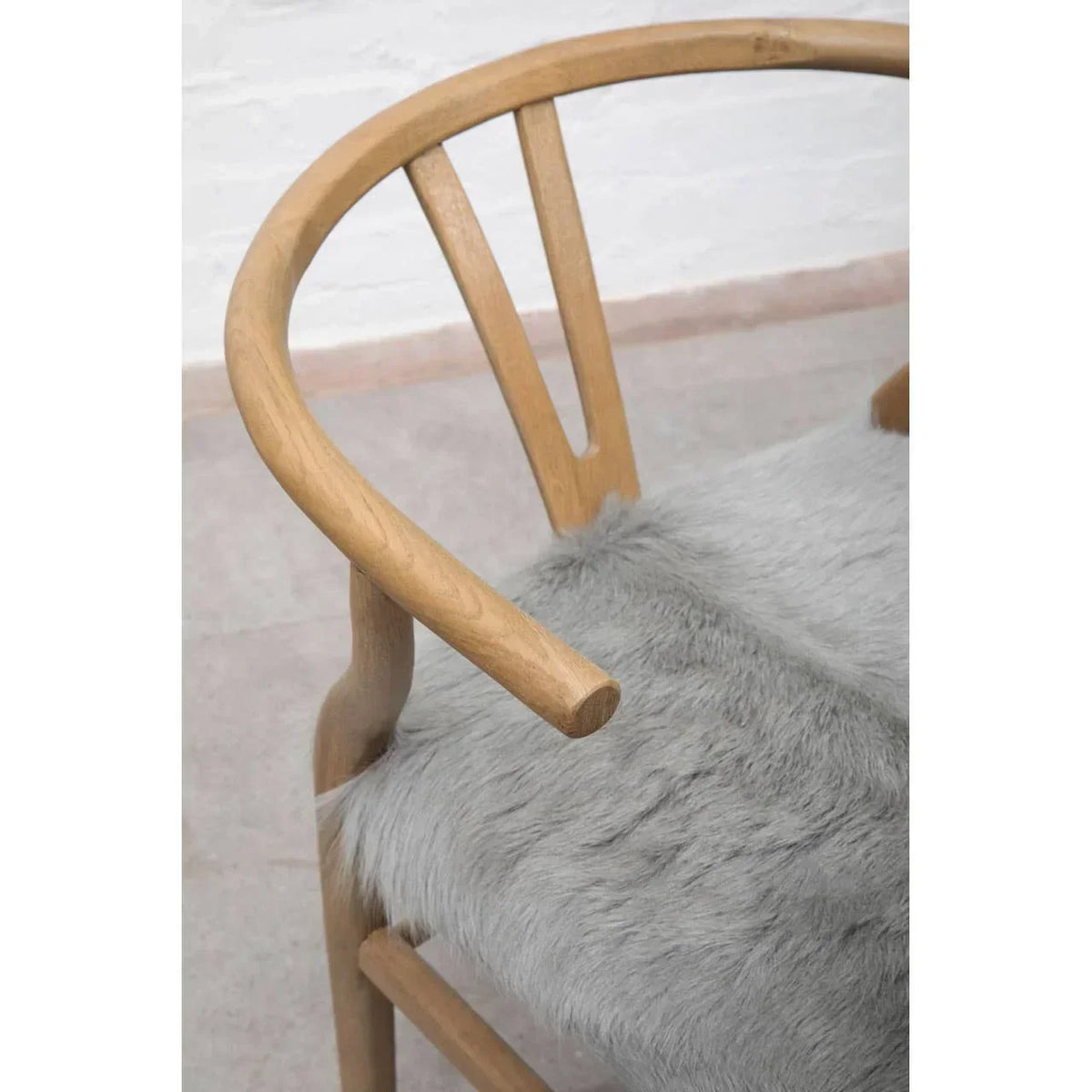 Curved wooden dining chair with light grey faux fur seat cushion, side angle view